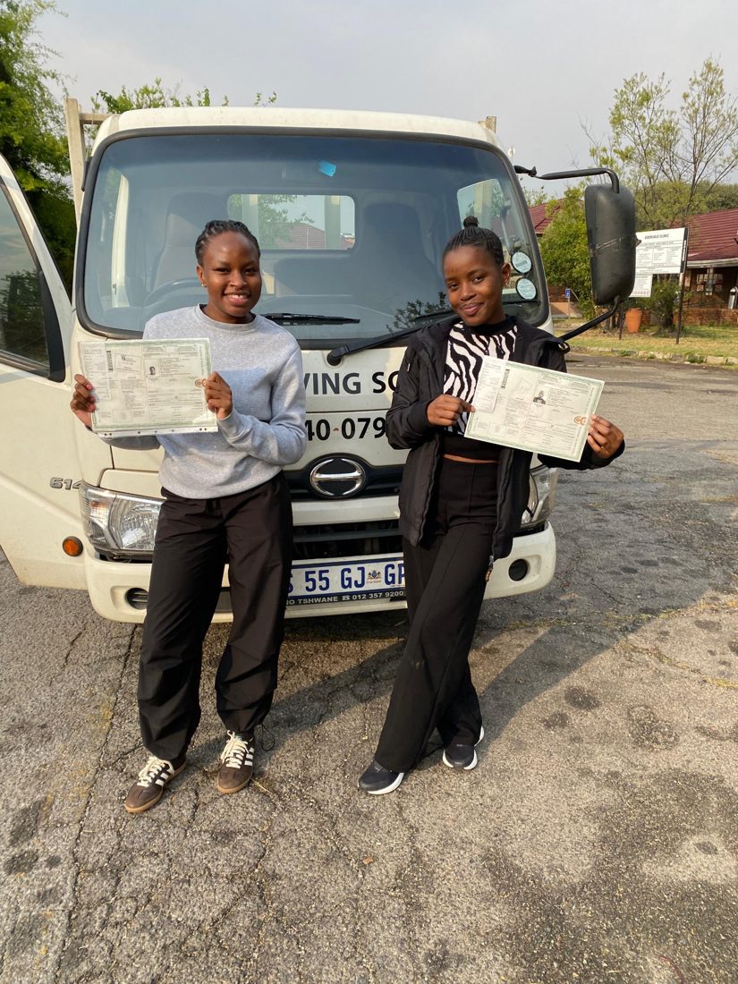 Two young learners smiling with their new licences in front of a 522 truck