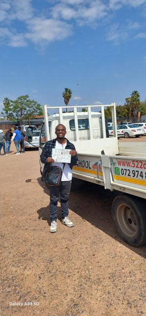 Smiling learner with his licence beside a 522 truck