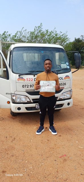 Learner holding his licence in front of a 522 truck