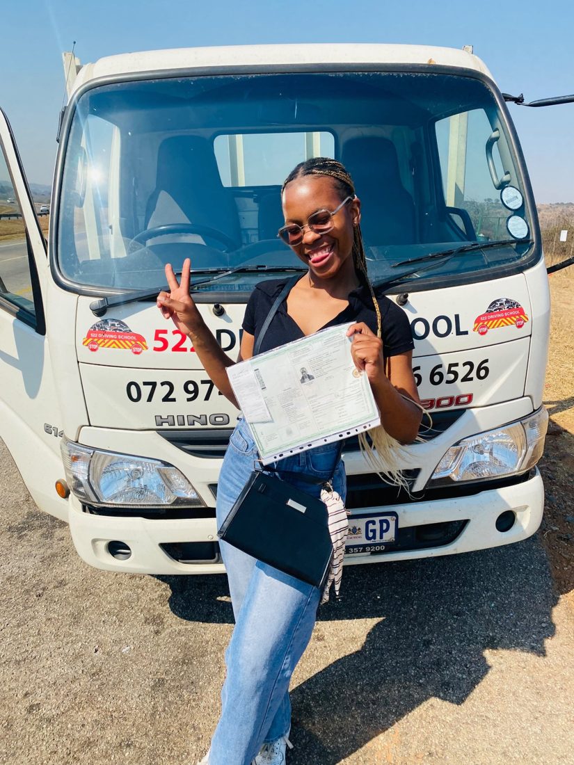 Smiling 522 learner holding her new licence in front of a 522 Driving School truck